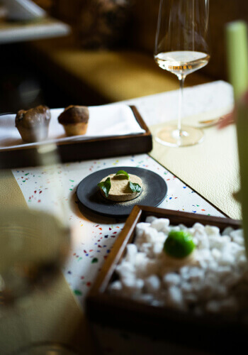 Fine dining table setting with gourmet dishes served on small plates and a glass of wine in a cozy upscale restaurant.