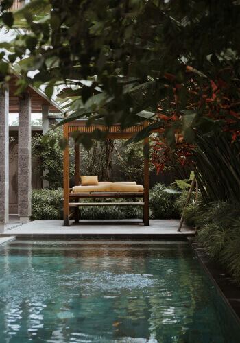 A private infinity pool next to a wooden canopy bed surrounded by lush greenery and a serene tropical atmosphere.